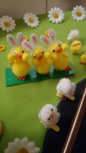 Easter decorations: yellow rabbits and fluffy chicks, large daisies and small yellow flowers on a green tablecloth.